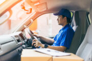 Young handsome delivery man driving his van with packages on the front seat