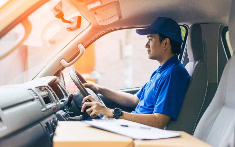 Young handsome delivery man driving his van with packages on the front seat