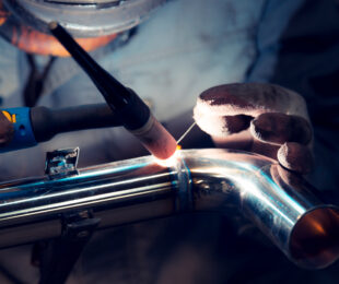 TIG welder welds elbow to polished stainless steel pipe