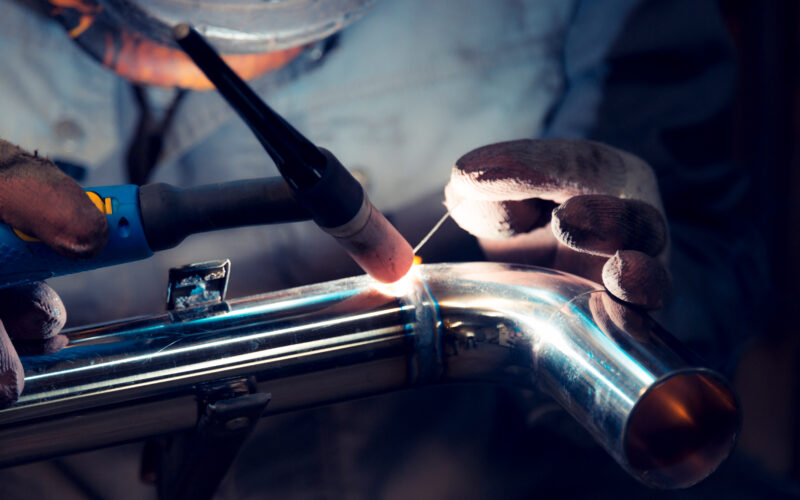 TIG welder welds elbow to polished stainless steel pipe
