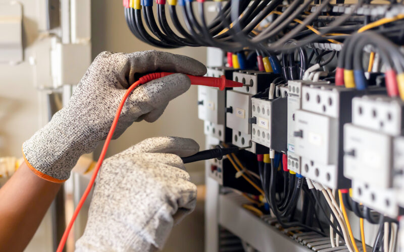 Electrician engineer uses a multimeter to test the electrical installation and power line current in an electrical system control cabinet.