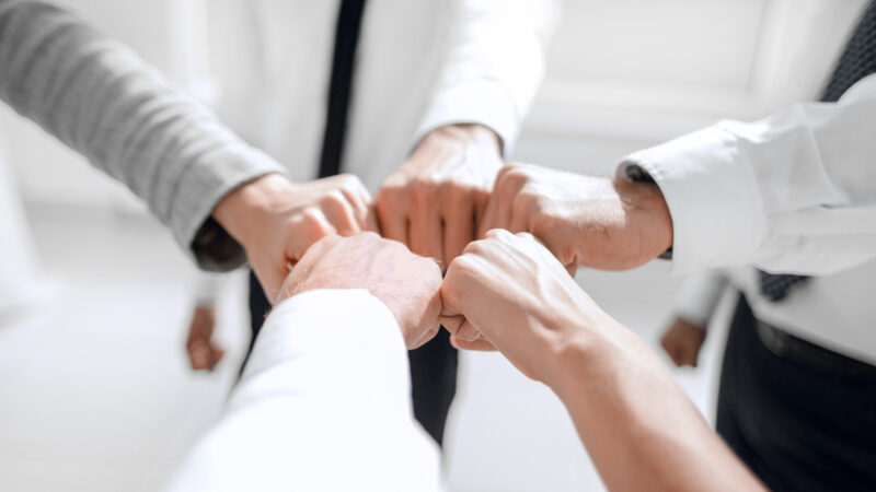 Close up of young businessman and businesswoman making a fist bump on building background